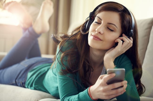 Attractive young woman with headphones listens music on smart ph