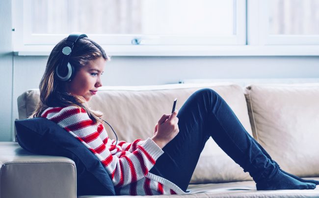 Teenage girls sits in sofa and listens to music or a podcast